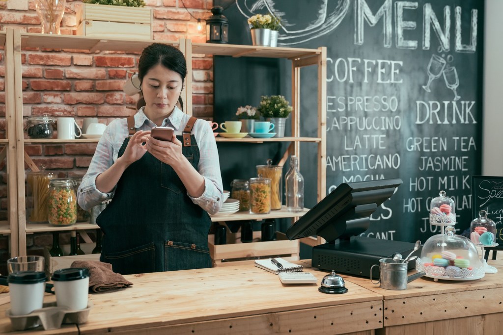 mulher ao celular em pé atrás de balcão