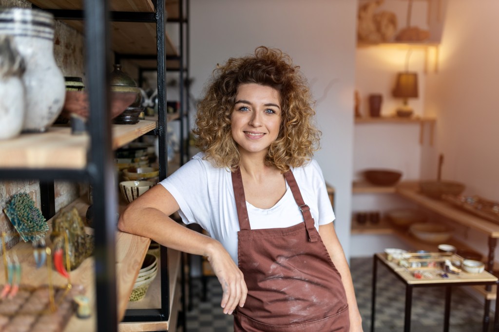 Mulher branca de avental posando para foto apoiada em prateleira