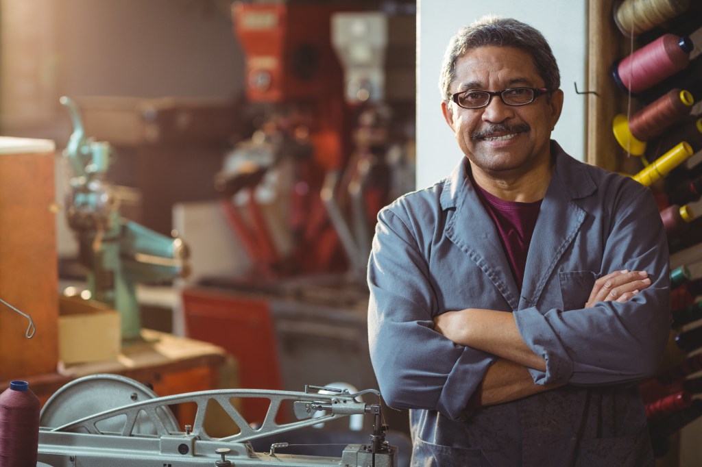 Trabalhador autônomo em pé rodeado de linhas de costura e máquinas